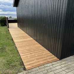 lang træterrasse langs sort hus med udsigt over vand