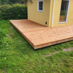 Lang træterrasse ved gult hus med flere havedøre