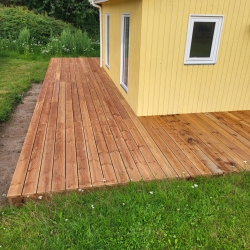 Lille træterrasse ved gult hus indgang med græ og småsten