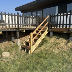 Træterrasse foran sort hus med trappe og siddeplads