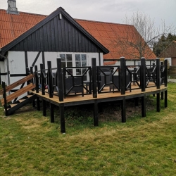 træterrasse foran sort træhus med sort rækværk og sandgrund
