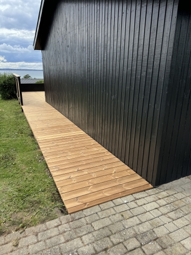 lang træterrasse langs sort hus med udsigt over vand