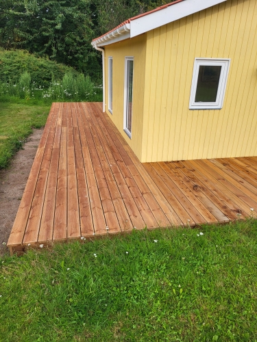 Lille træterrasse ved gult hus indgang med græ og småsten