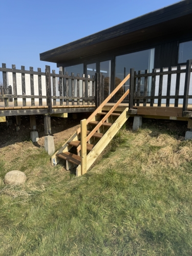 Træterrasse foran sort hus med trappe og siddeplads