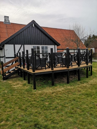 træterrasse foran sort træhus med sort rækværk og sandgrund