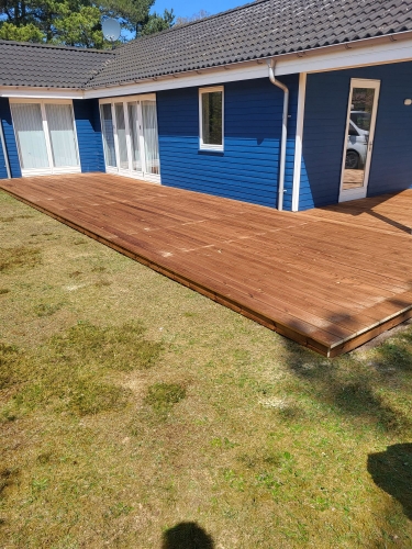 træterrasse ved blåt hus med havedøre og hvid tagrende